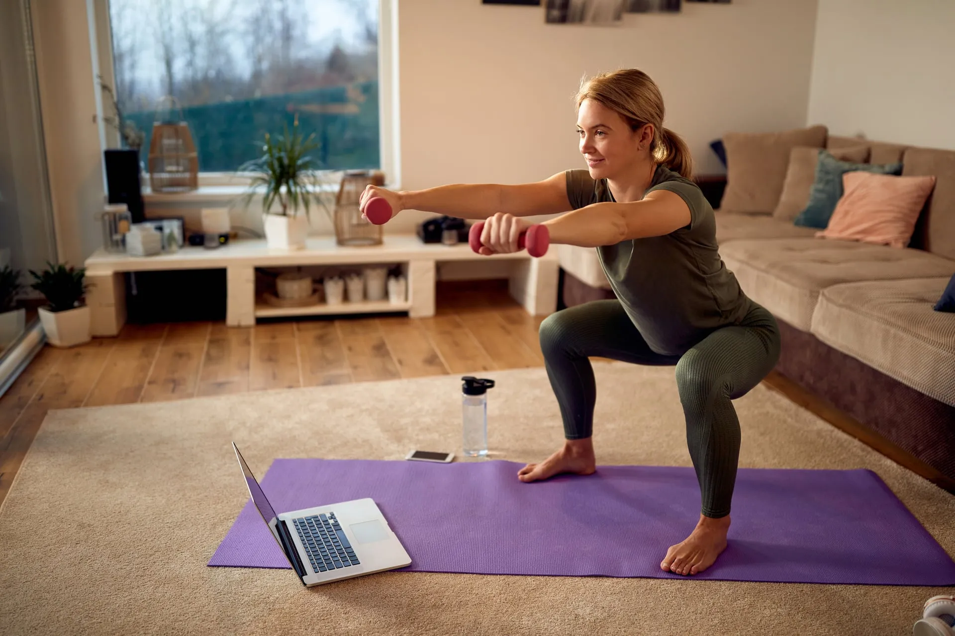 Mujer entrenando con mancuernas frente a un portátil siguiendo una sesión online
