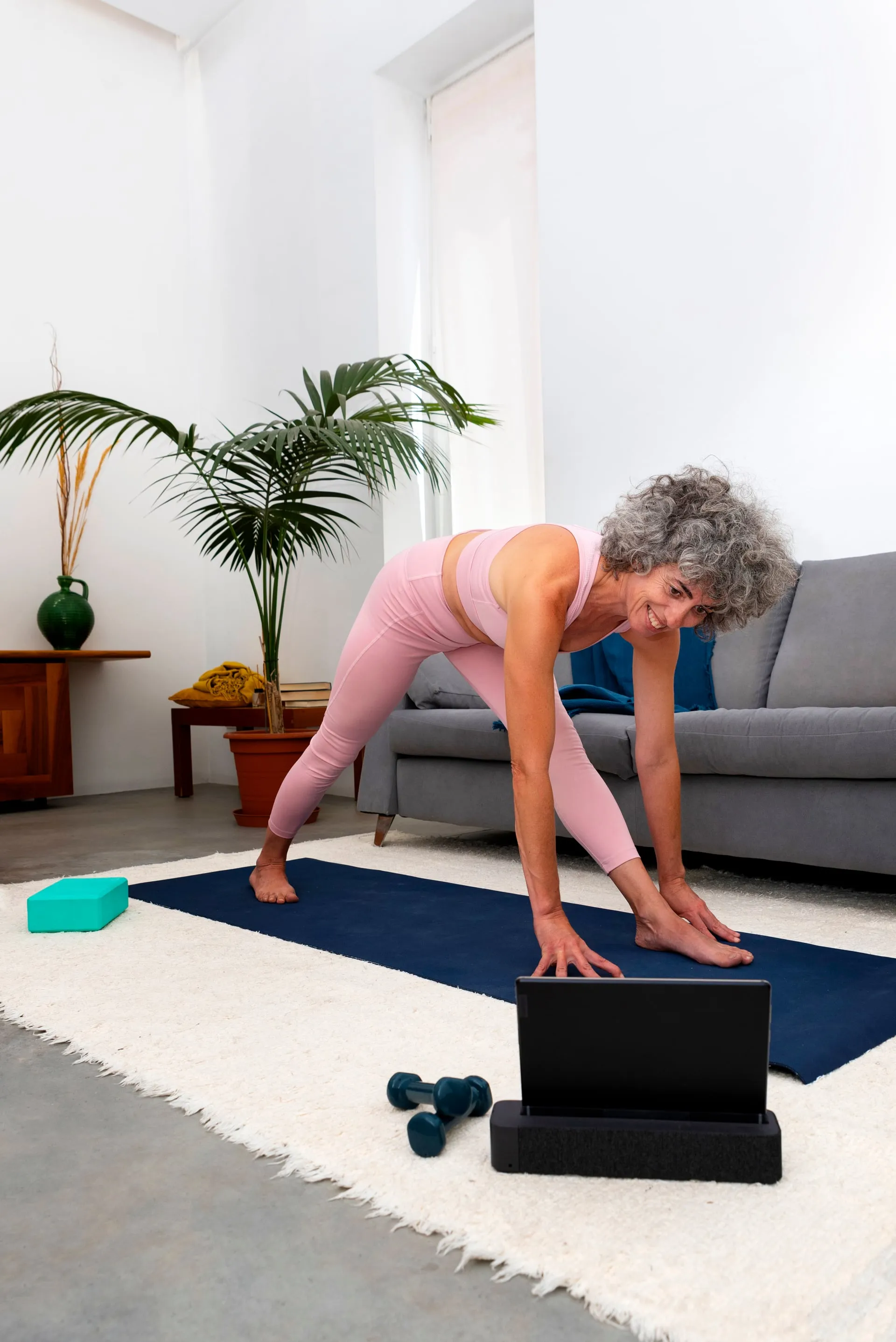 Mujer mayor entrenando frente a una tablet en su salón con luz natural