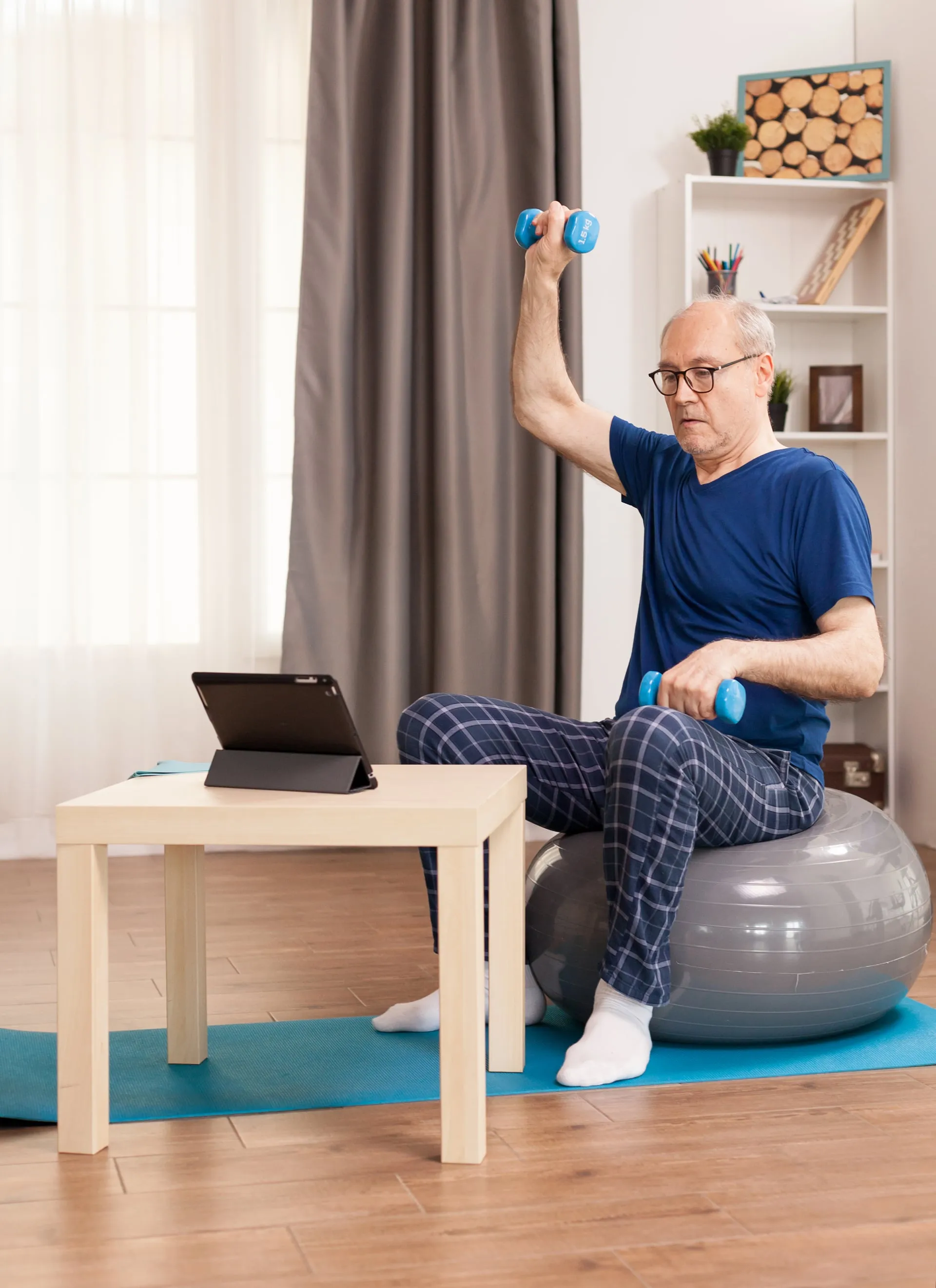 Hombre mayor entrenando con mancuernas frente a una tablet en sesión online